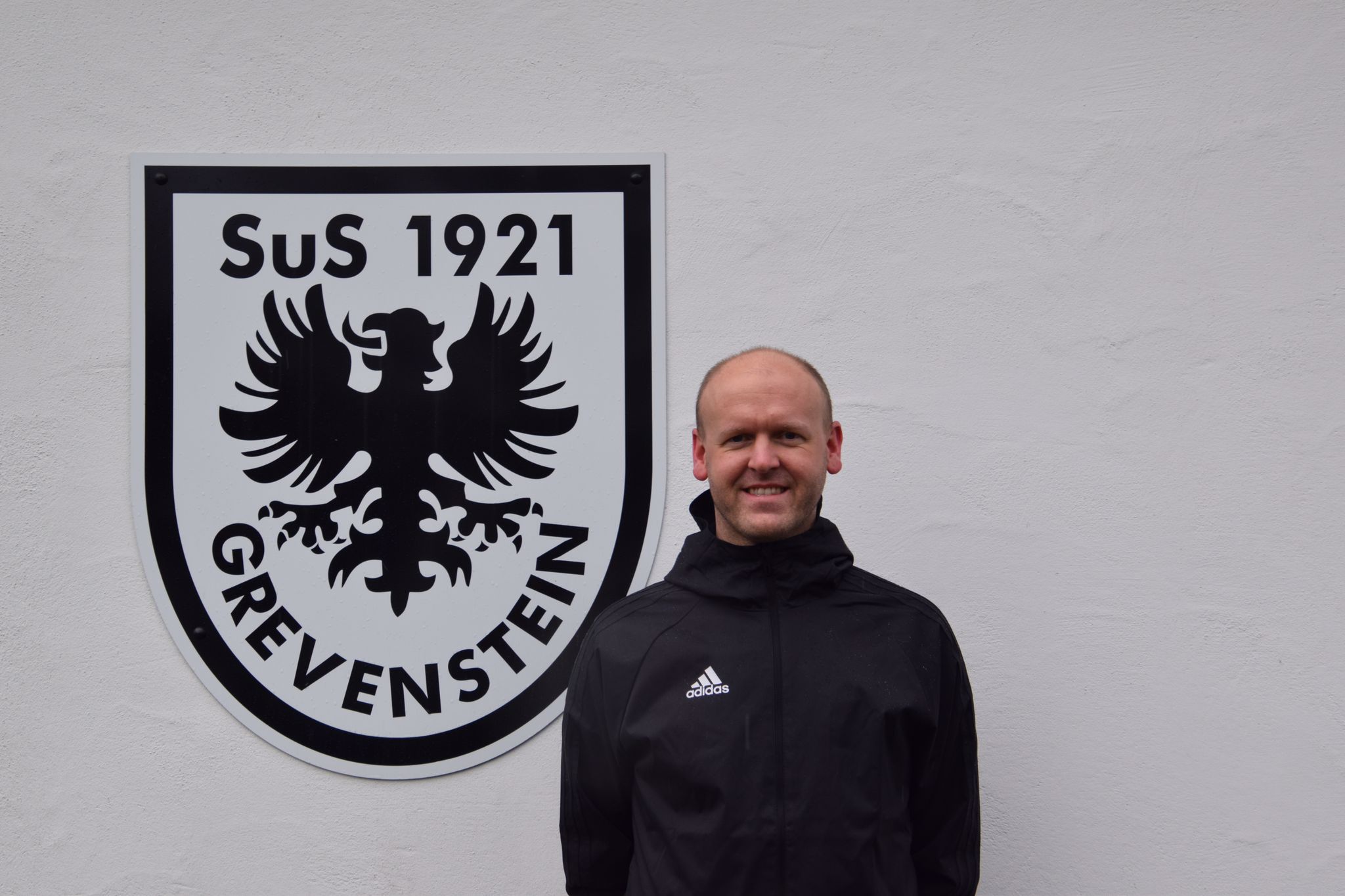 Sebastian Vedder vor dem SuS Grevenstein-Wappen am Sportheim
